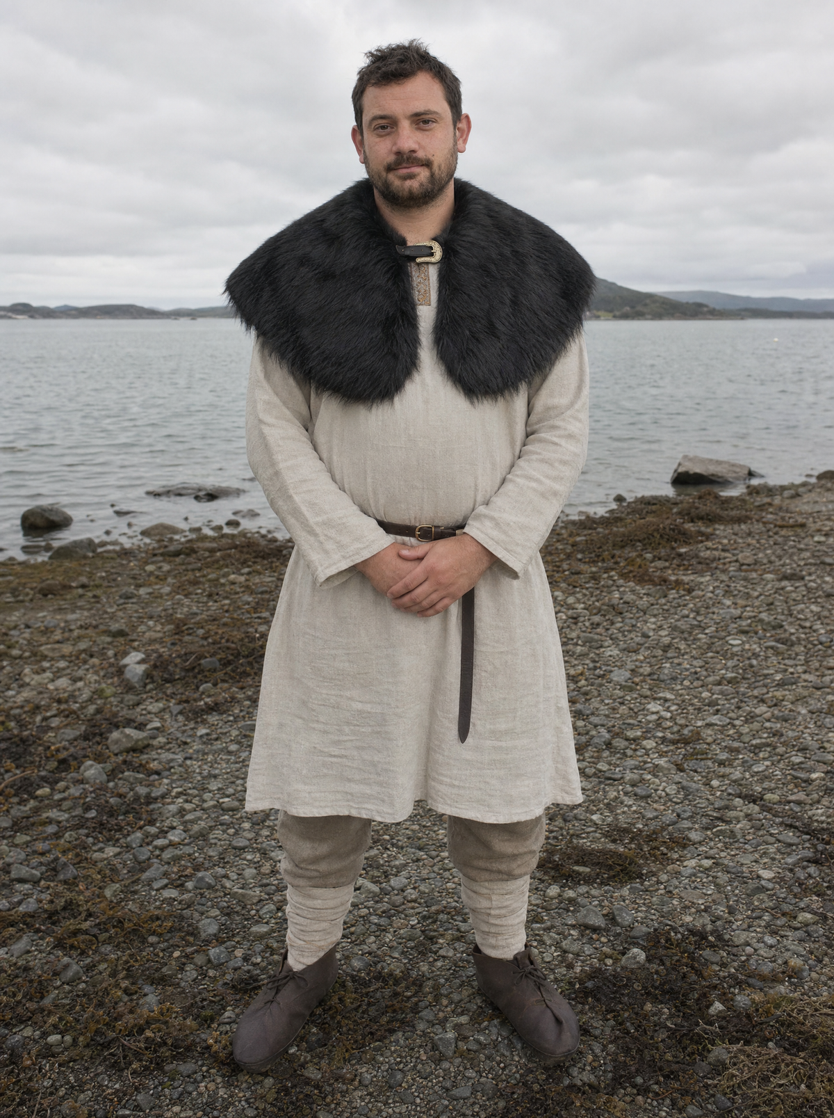 Man in a cream tunic with a thick black faux fur shoulder cape by the sea