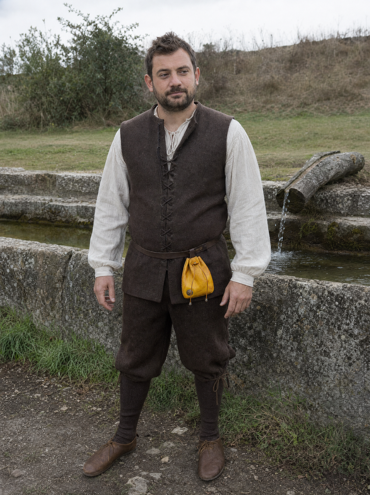 Man in a white shirt and dark vest with a small yellow leather coin pouch on his belt