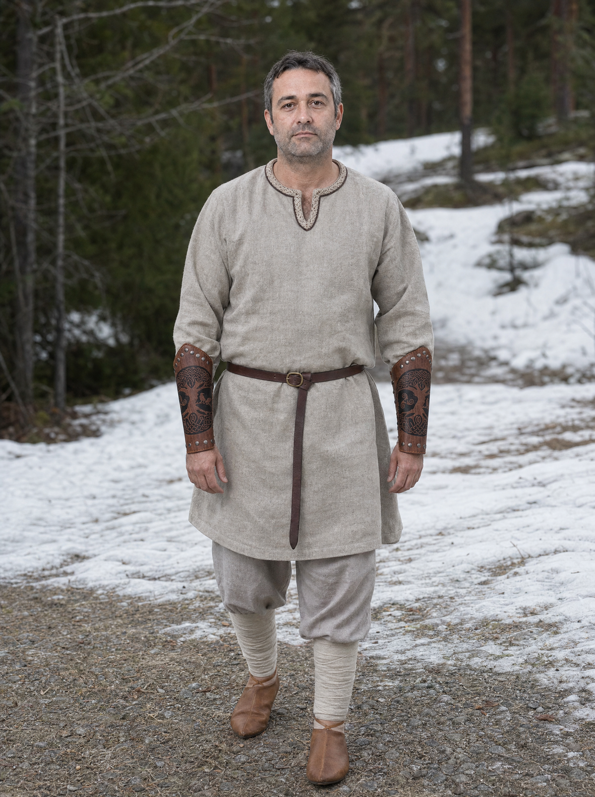 Man in a pale tunic wearing riveted faux leather bracers on a snowy path