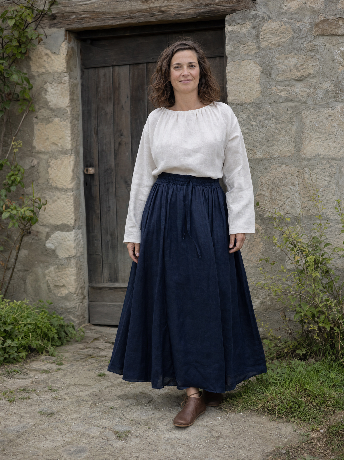 Woman in a white blouse and a long navy ramie skirt by a stone doorway