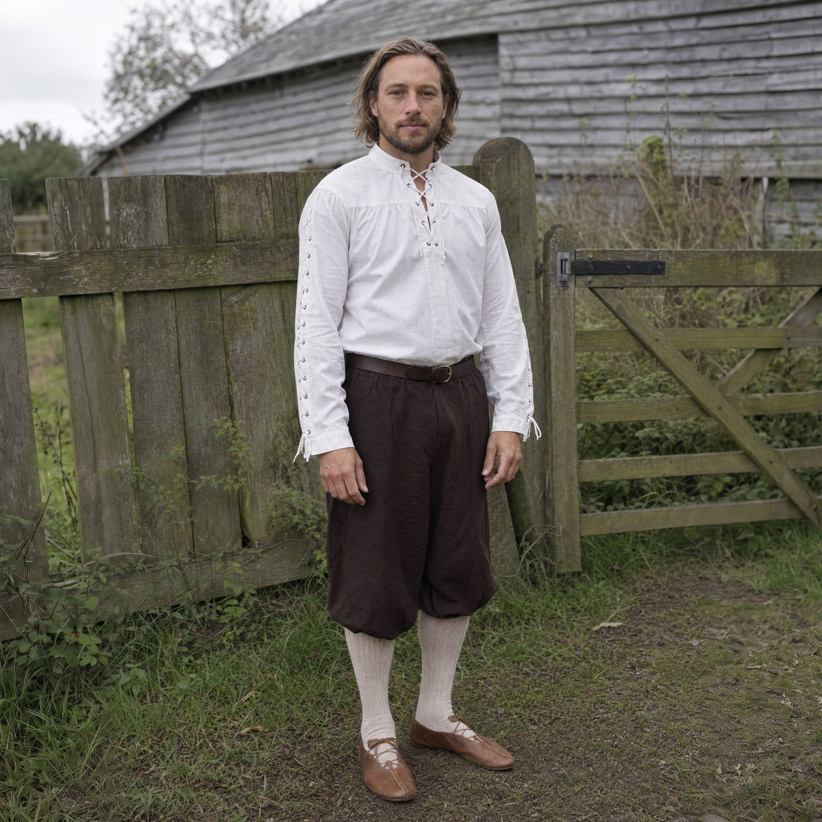 A man in the Renaissance Gentleman look outdoors: white laced shirt and dark trousers