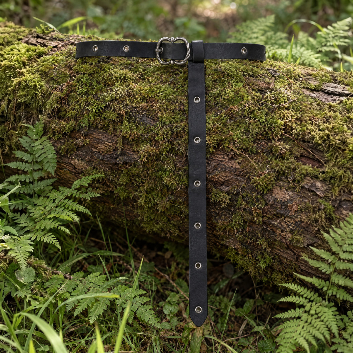 Black eyelet belt with ornate buckle on a rustic surface