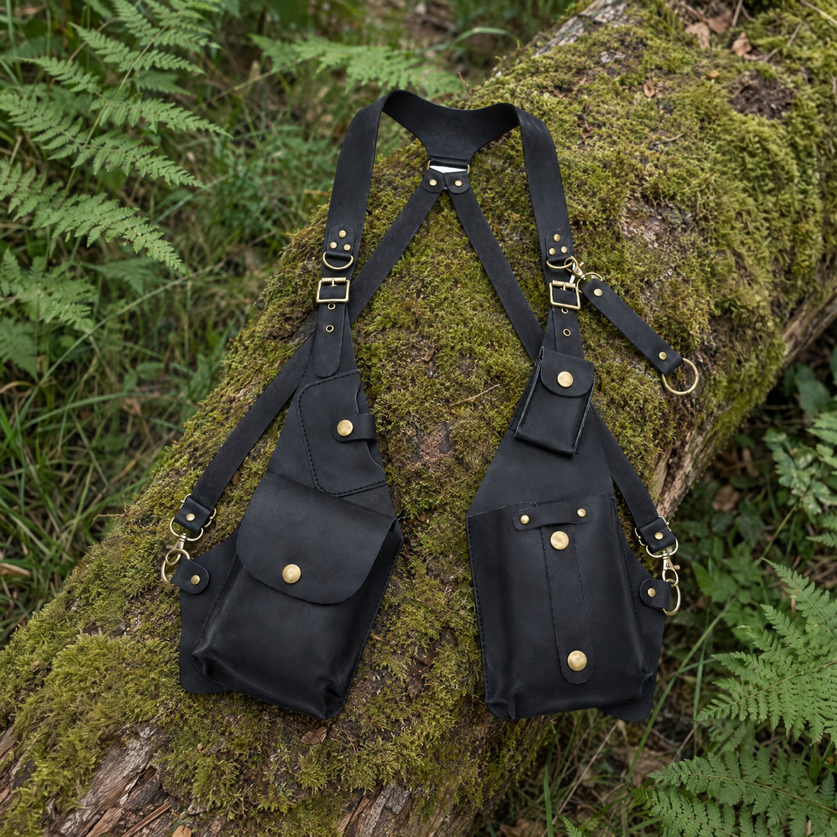 Black faux leather shoulder straps with underarm pouches on a rustic surface