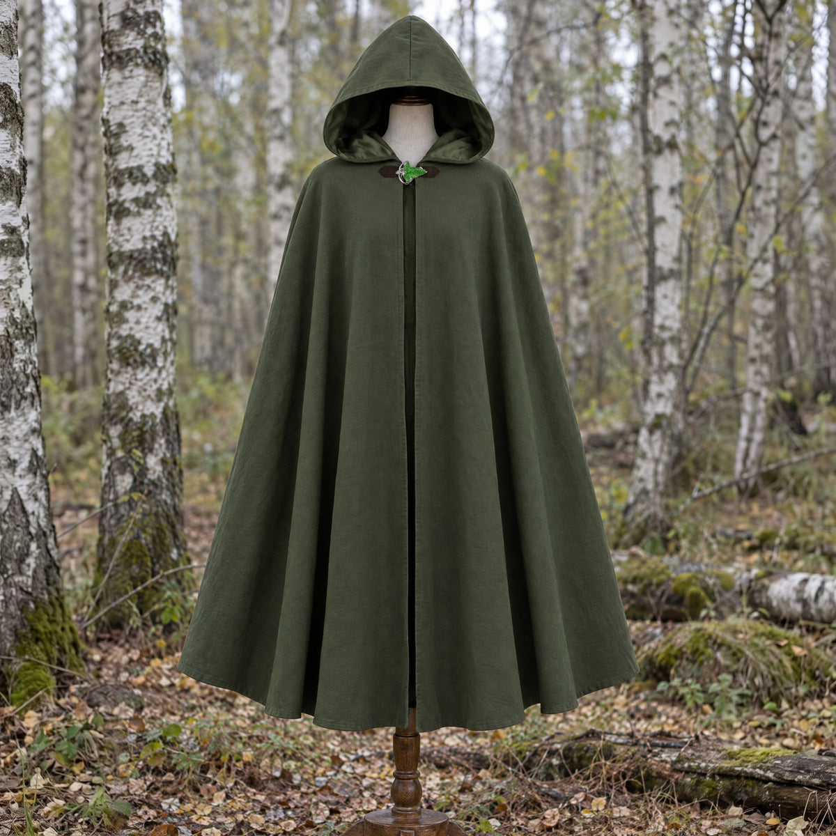 Green hooded cloak with leaf brooch on a dress form outdoors
