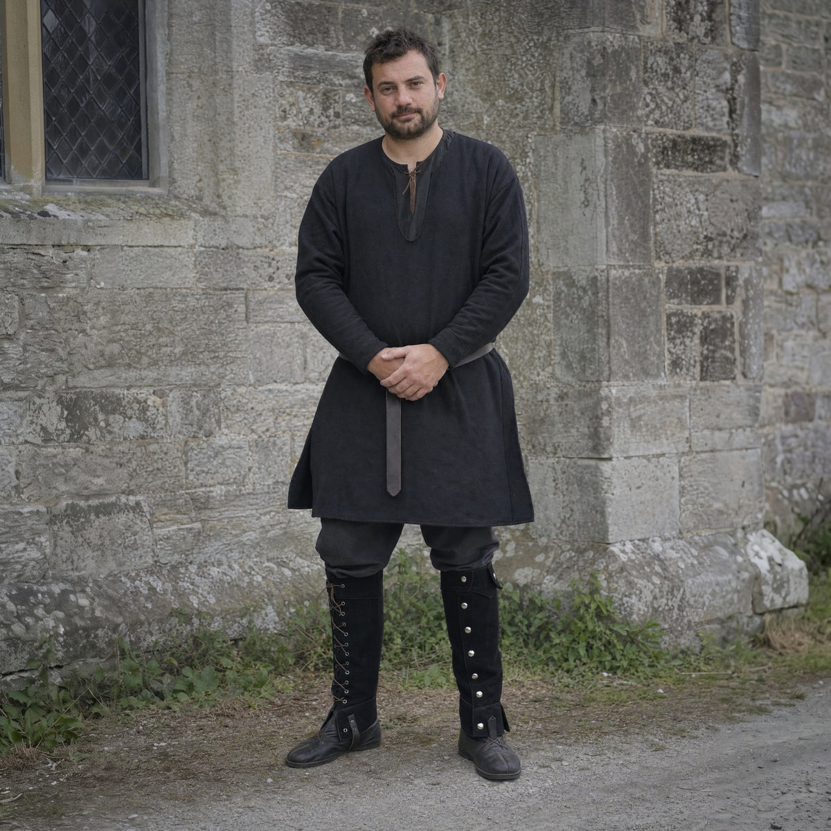 Black lace-up studded gaiters worn over boots outdoors, full-length front view