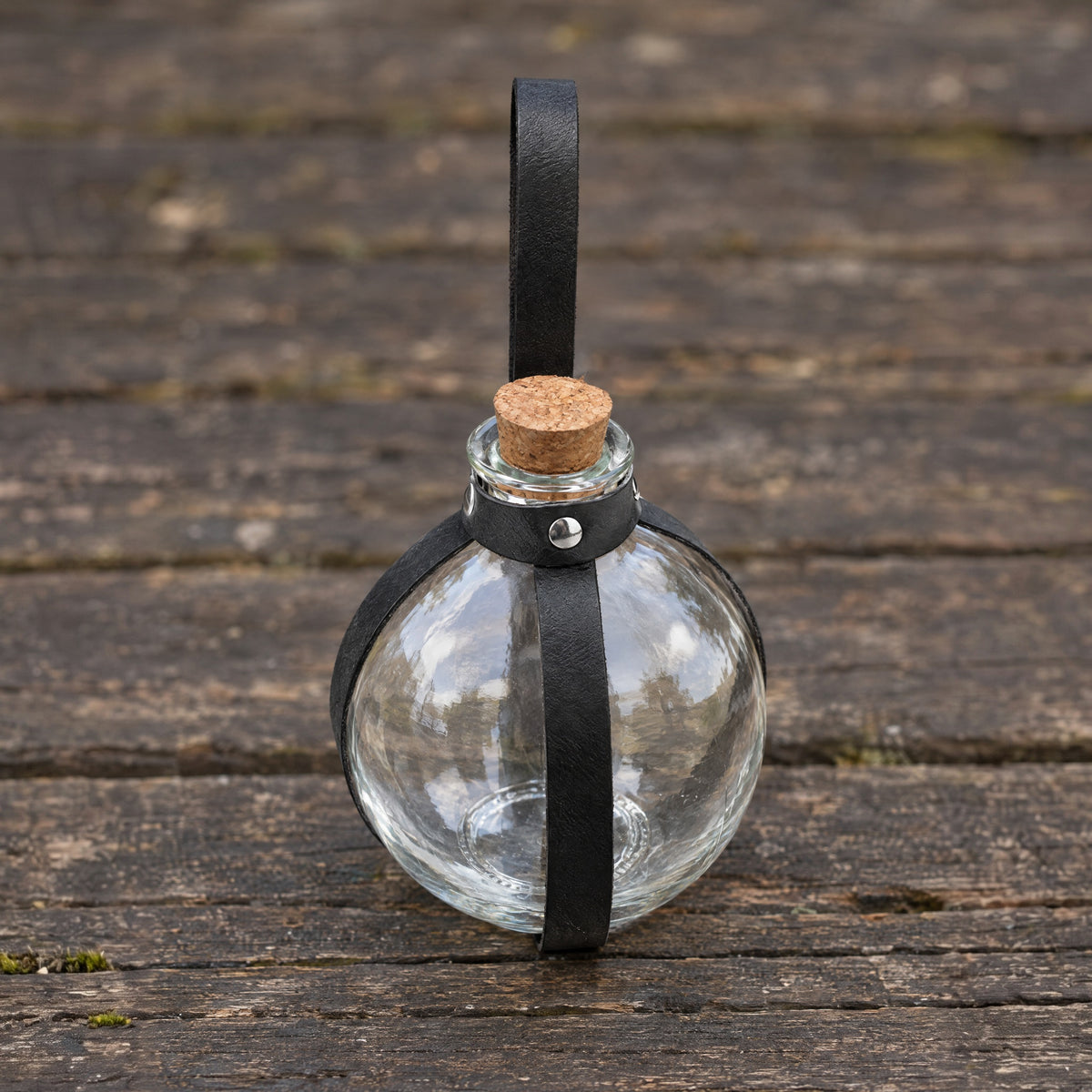 Black round potion bottle with belt holder on a rustic surface