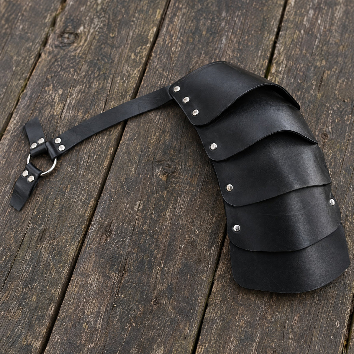 Black segmented single pauldron on a rustic surface