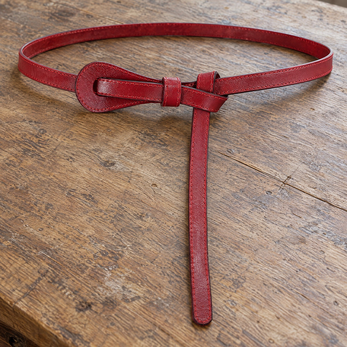 Red slim leather tie belt on a rustic surface