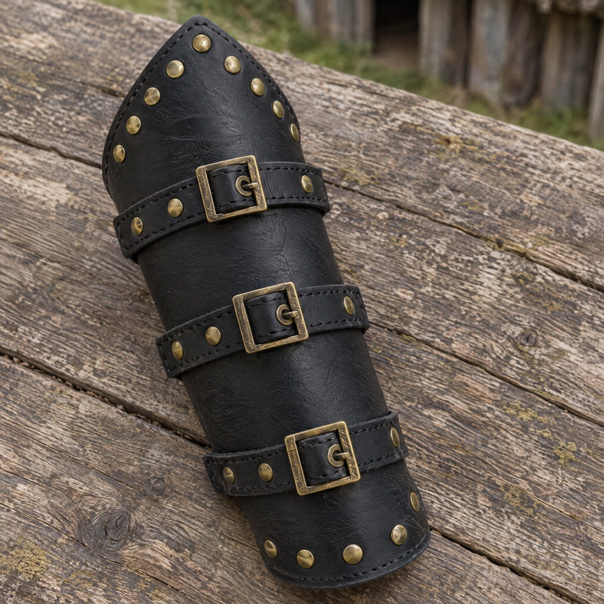 Black studded brass-buckle Viking bracer on a rustic surface