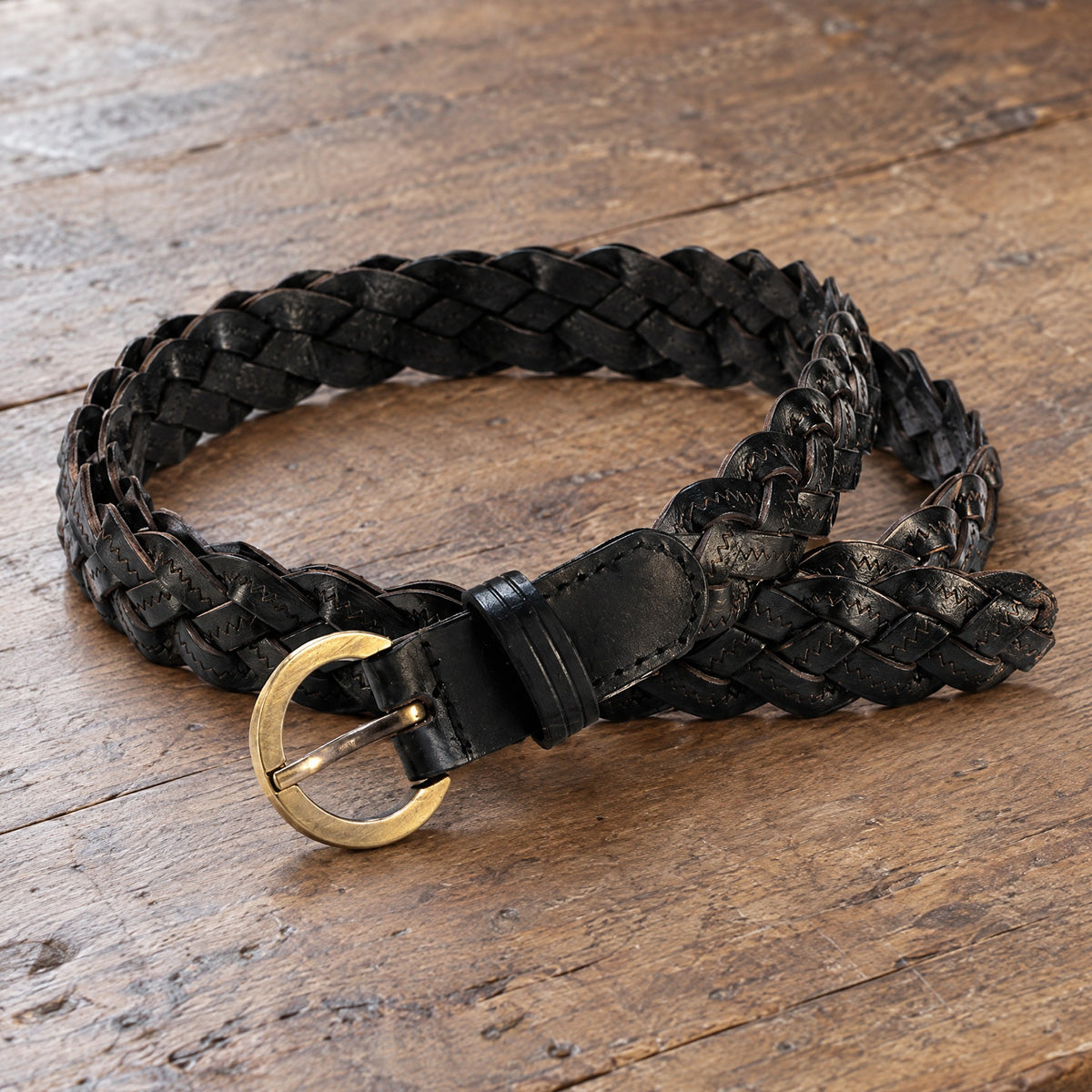 Black thin braided leather belt on a rustic surface